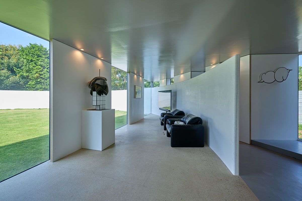 リビング。外の塀が屋内にまで入り込んでいる。床も壁も、名のある左官が仕上げた美術品でもある。窓から見える借景の緑も気持ちよい。