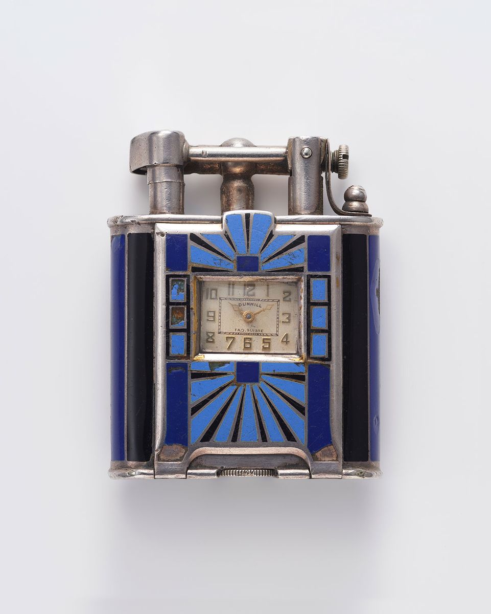 片手で扱えるコンパクトさで人気を博したライター。はっきりした発色のエナメルと銀の直線で構成される明快な装飾は、アール・デコのスタイルをよく表している。時計付きライター ダンヒル社 1920年代 個人蔵　撮影:若林勇人
