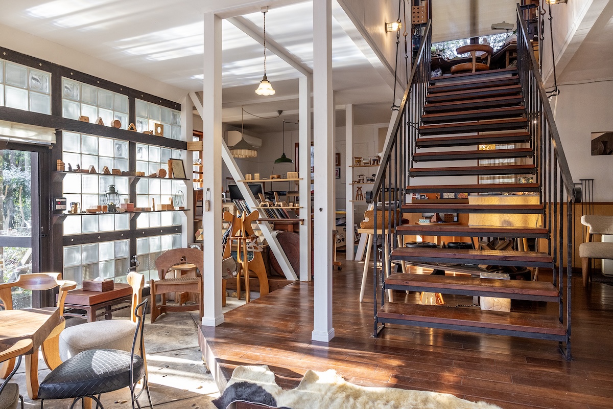 アトリエの入口より全体を望む。壁の一部はガラスブロックが用いられ明るく開放的な雰囲気。左奥に手がけた椅子たちが見える。