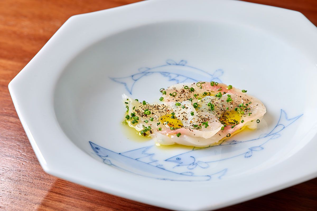 北イタリアのトレンティノ=アルト・アディジェ州の郷土料理をベースにした「トラフグのカルネサラータ」。本来は牛もも肉を熟成させる料理だが、厚く引いたトラフグを使い、岩塩、ニンニク、ローズマリーとジュニパーベリーとともに寝かせて旨みを引き出した。