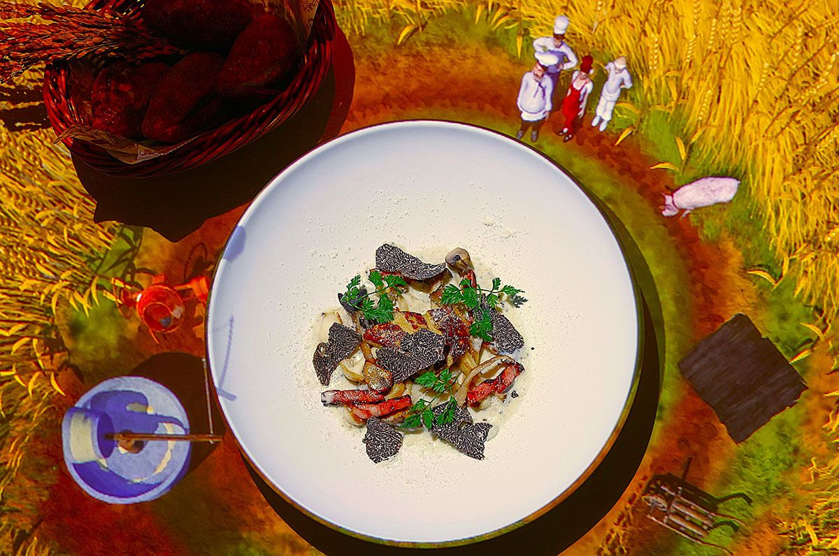 料理はすべてレギュラーコース2万4000円より。「トリュフ豚が掘り当てたトリュフを使用したラビオリ」。テーブルに投影されているのはイタリア・トスカーナの小麦畑。